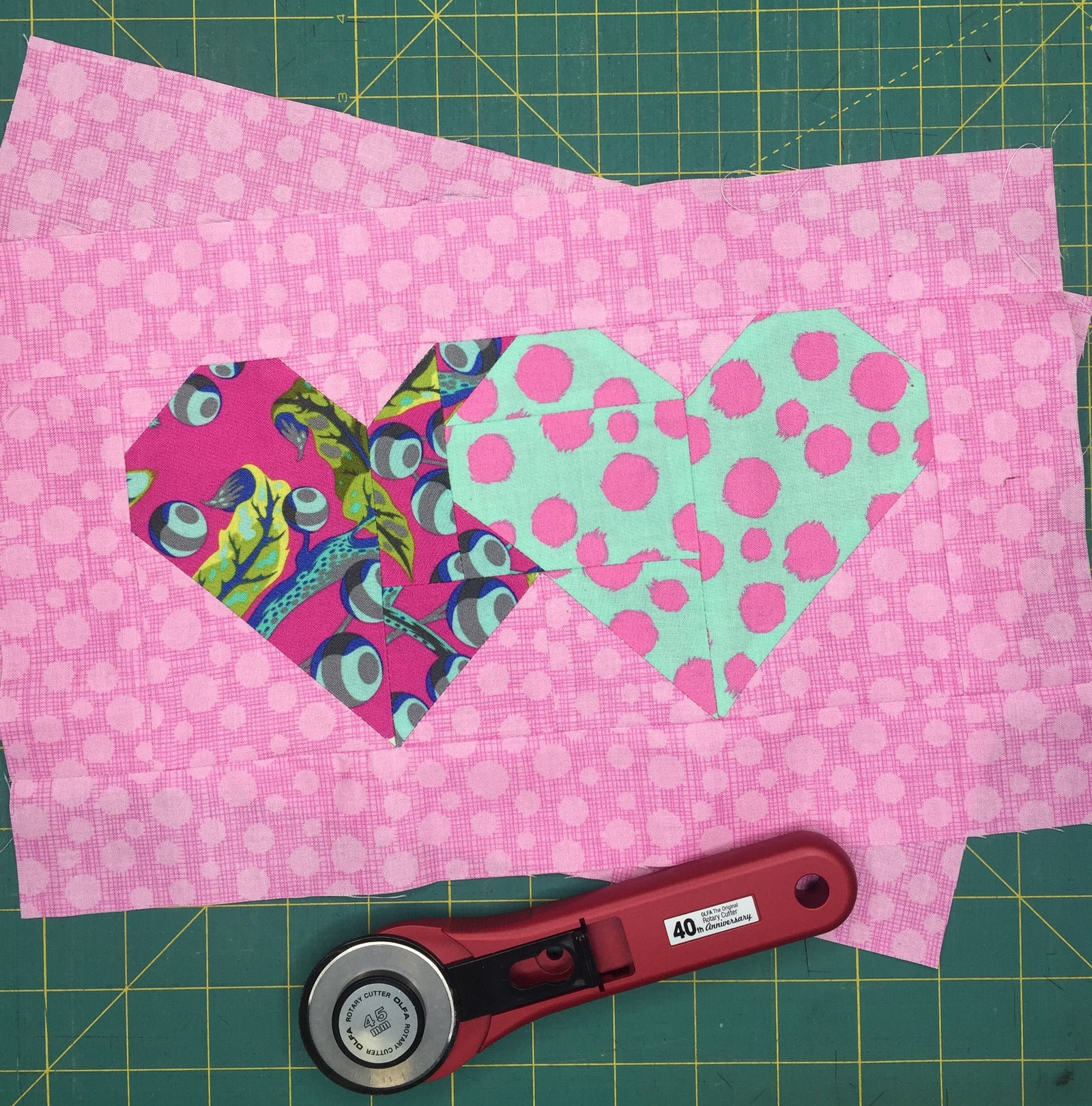 A pink and blue heart quilt with a red rotary cutter.