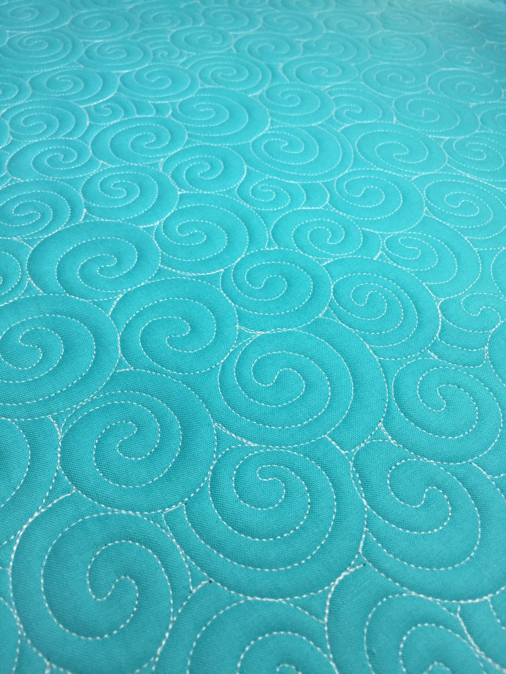 Turquoise fabric with swirling stitched patterns.