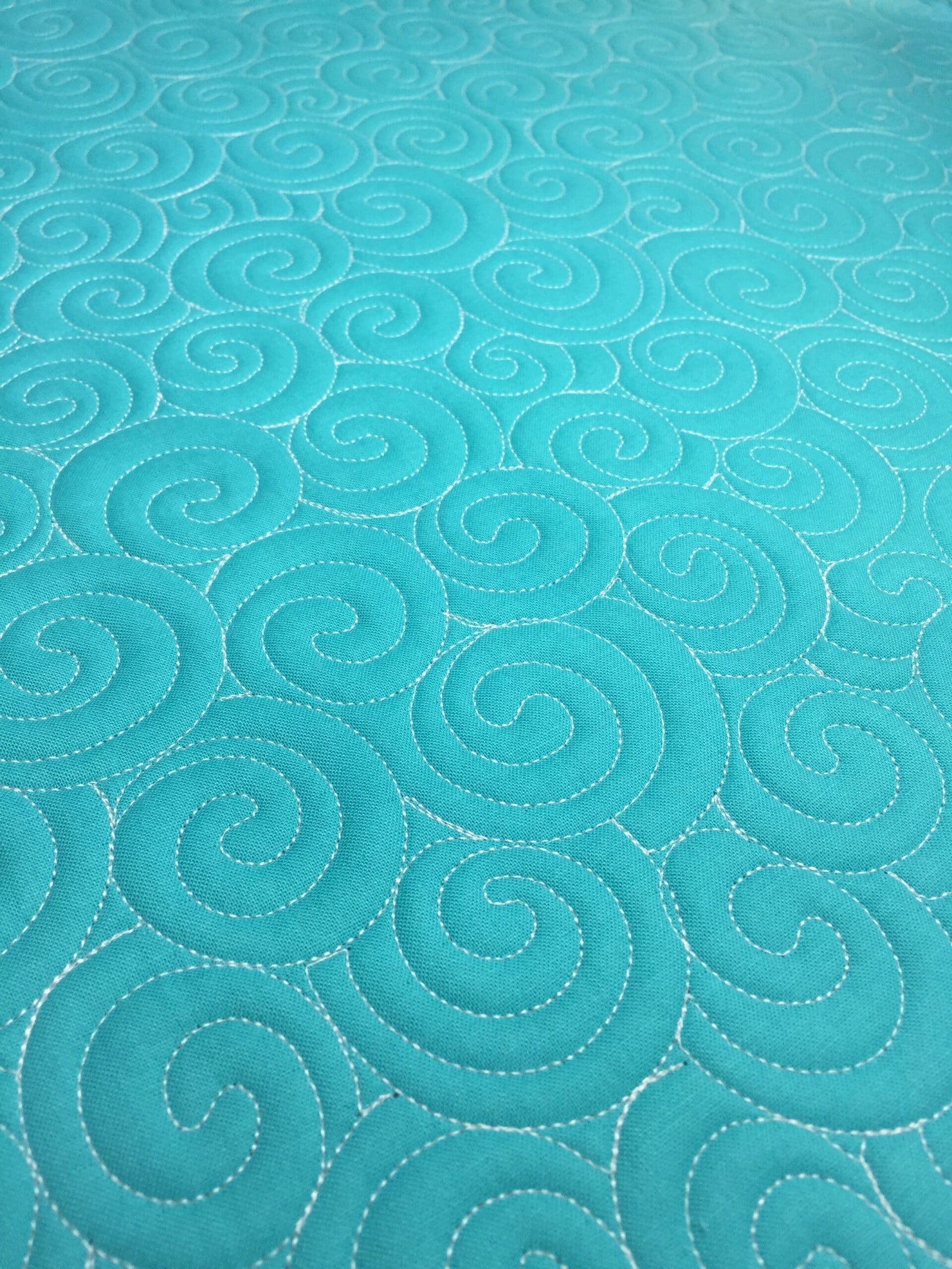 Turquoise fabric with swirling stitched patterns.