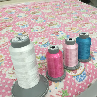 Four sewing thread spools on pink cupcake fabric
