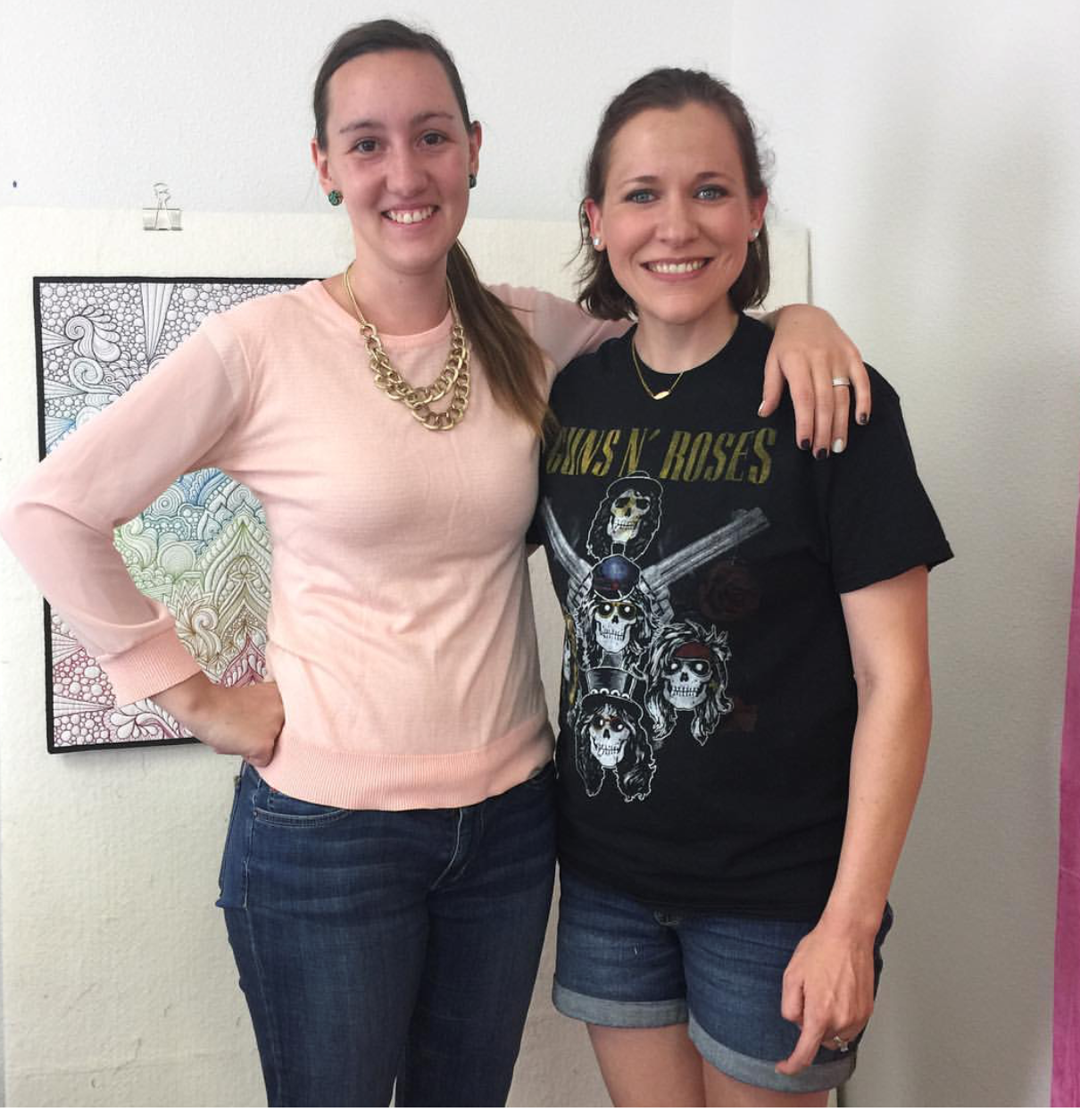 Two women standing next to each other in front of a wall.