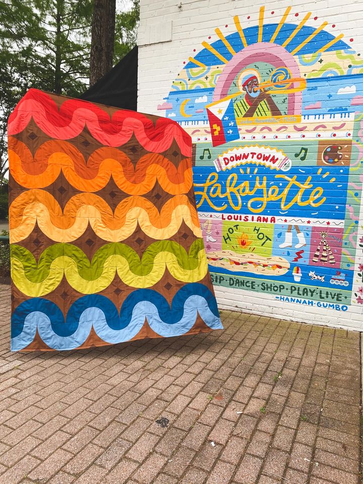 A colorful quilt is on display in front of a building.