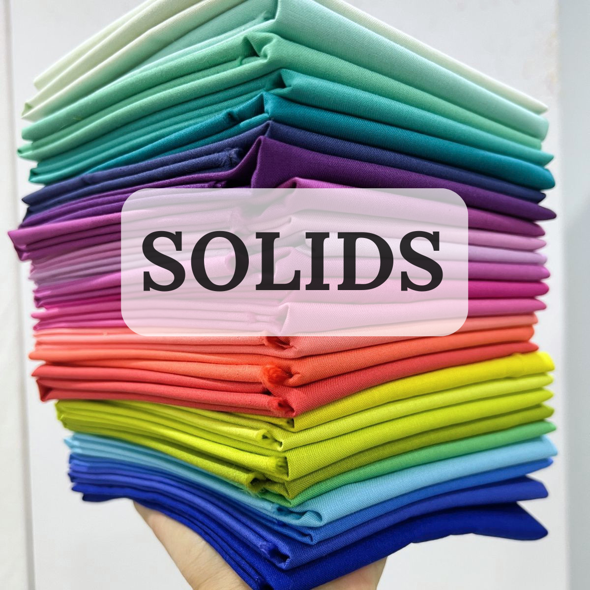 a hand holding up a bundle of bright colored fat quarters of fabric with the word Solids on the image