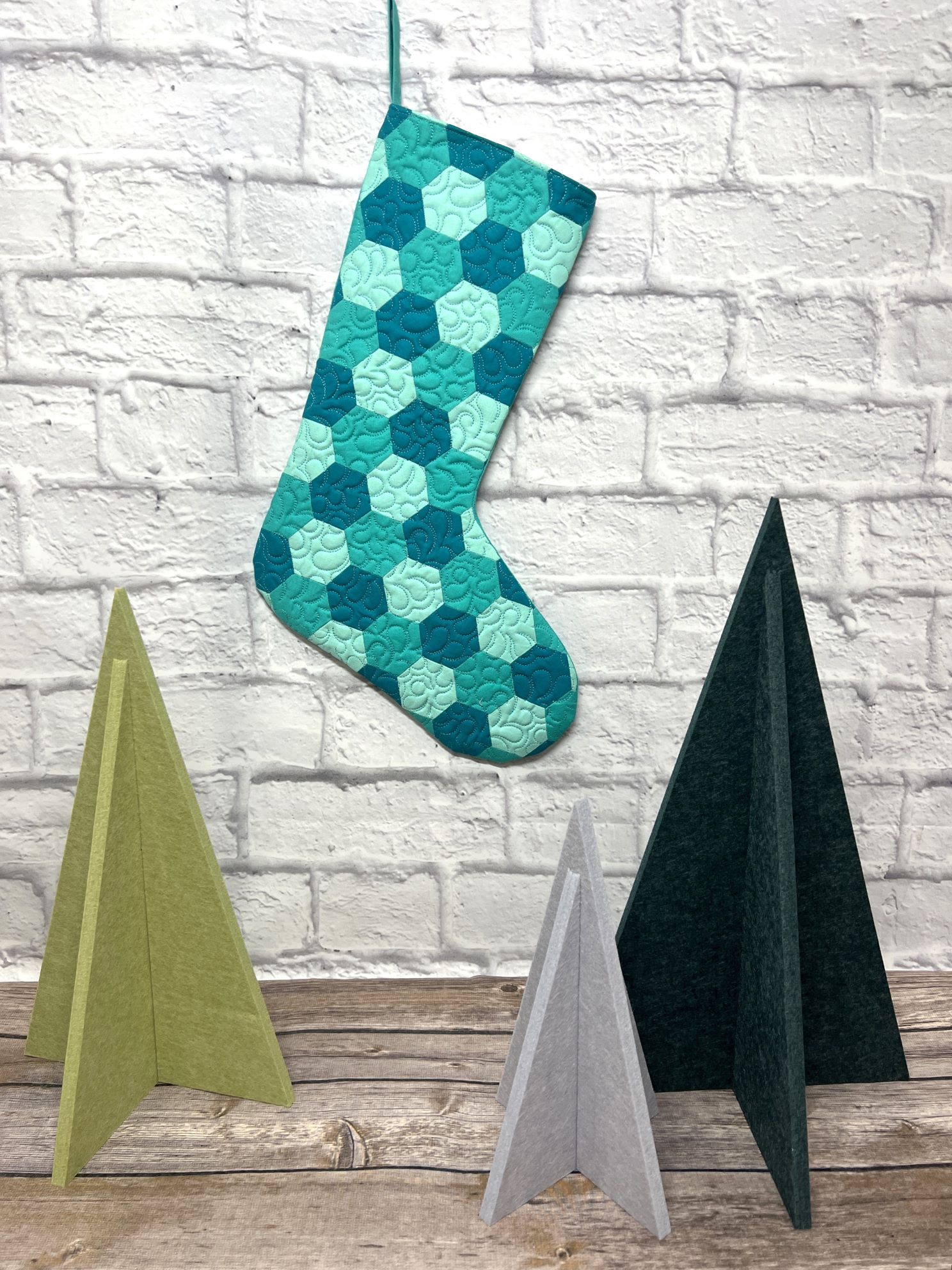A blue stocking hanging on the wall next to three other christmas trees.