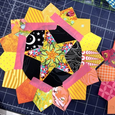 Colorful patchwork quilt block with star and heart shapes on a cutting mat.