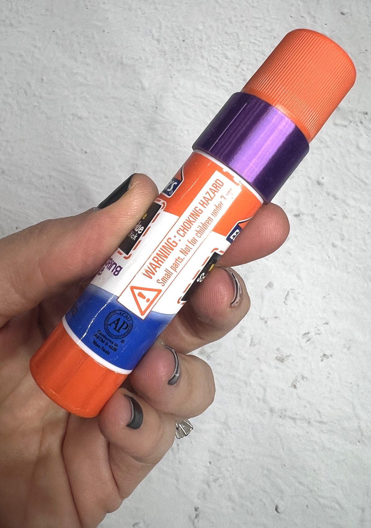 Hand holding a purple and orange spray can with warning labels.