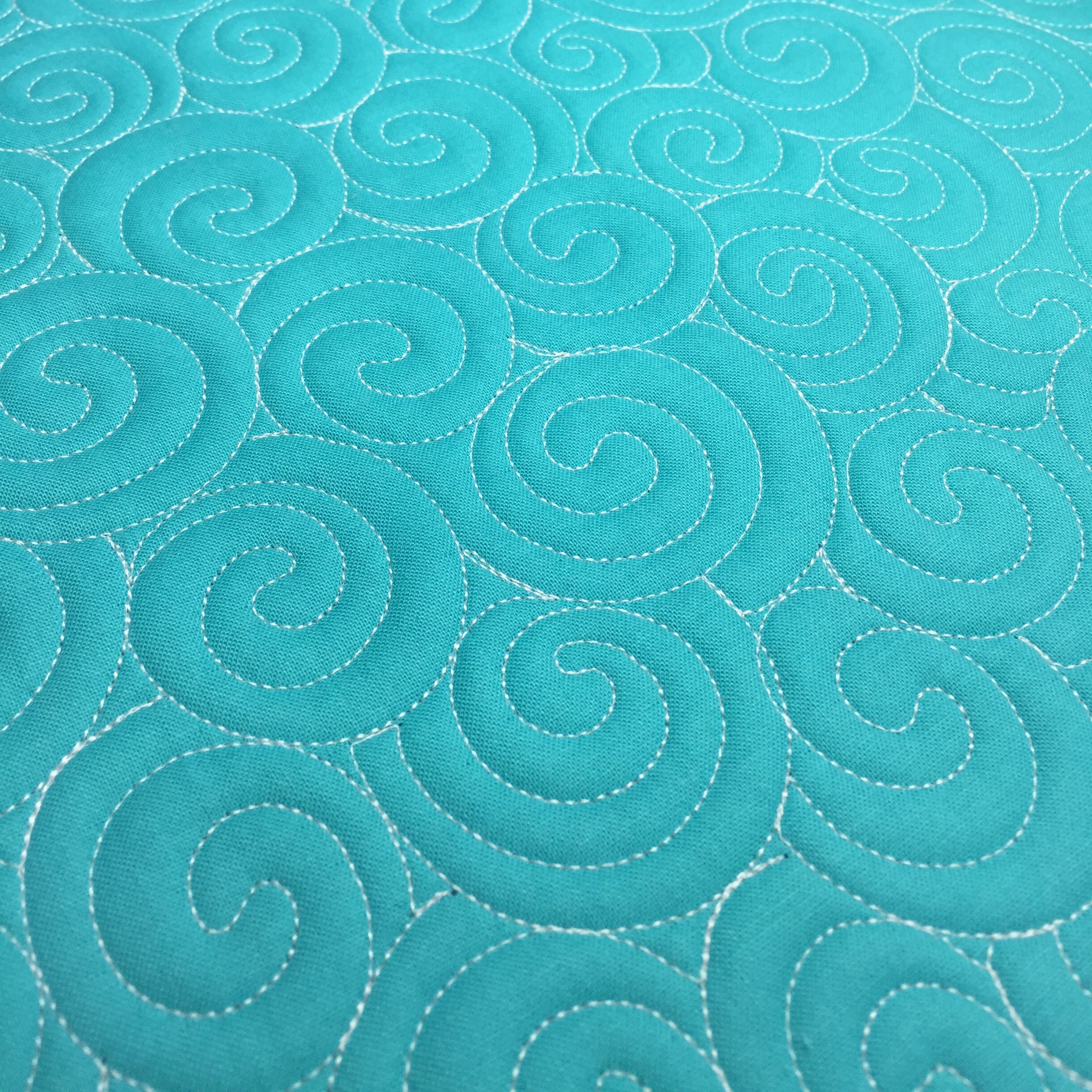 A close-up of turquoise fabric with a repeating quilted swirl pattern stitched in white.