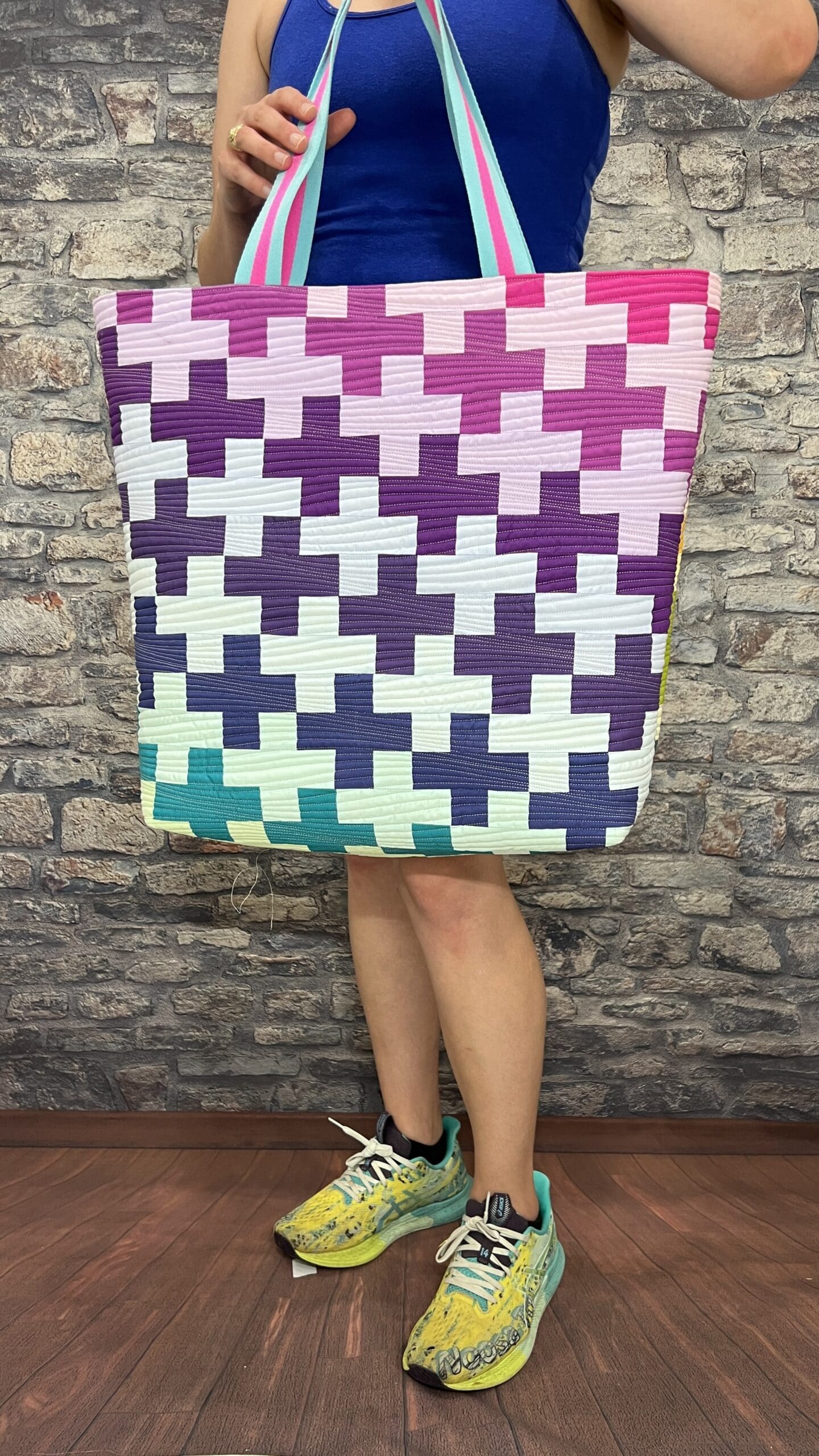 A person standing in front of a brick wall holding up a quilt.