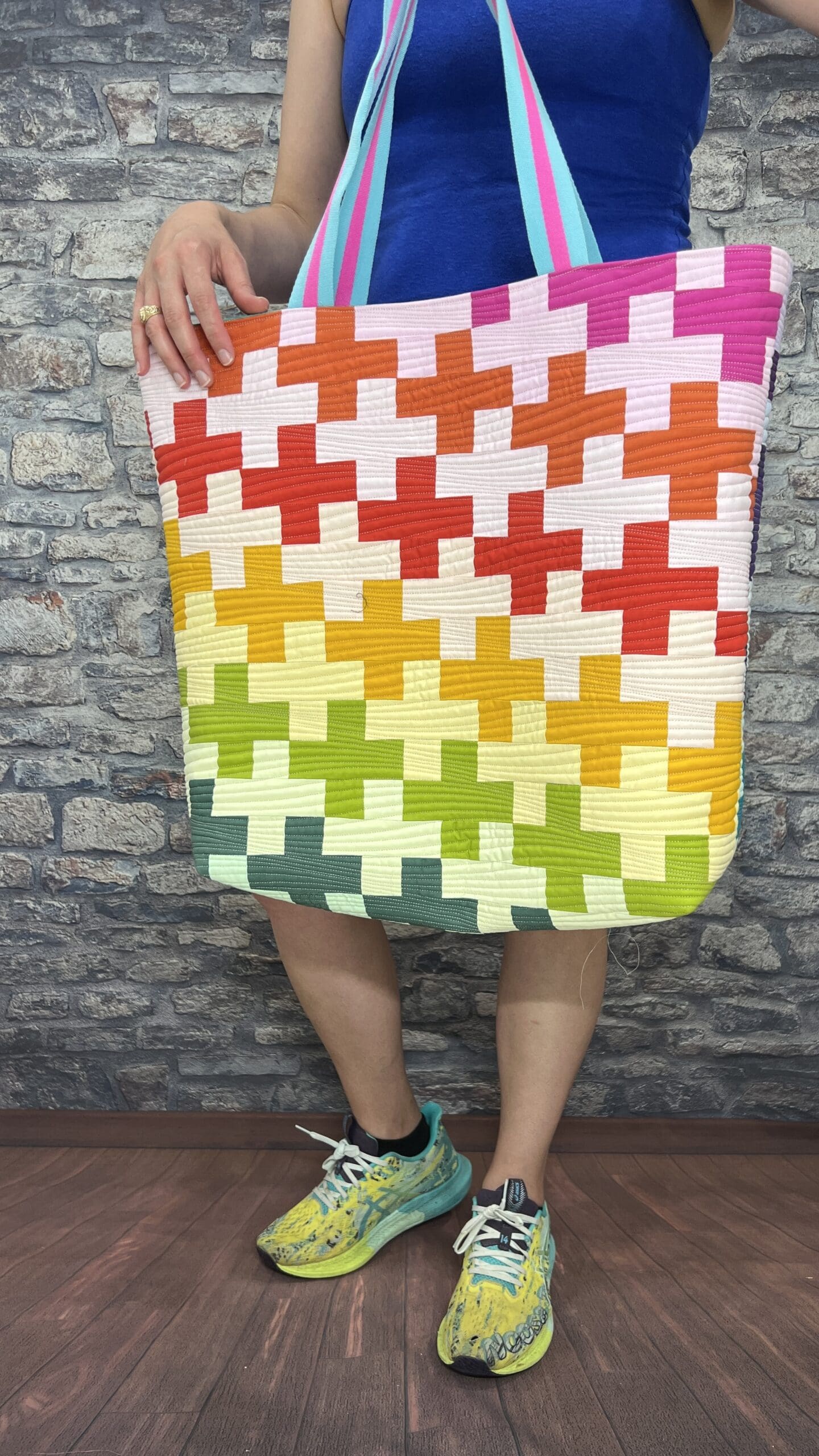 A person standing in front of a brick wall holding up a quilt.