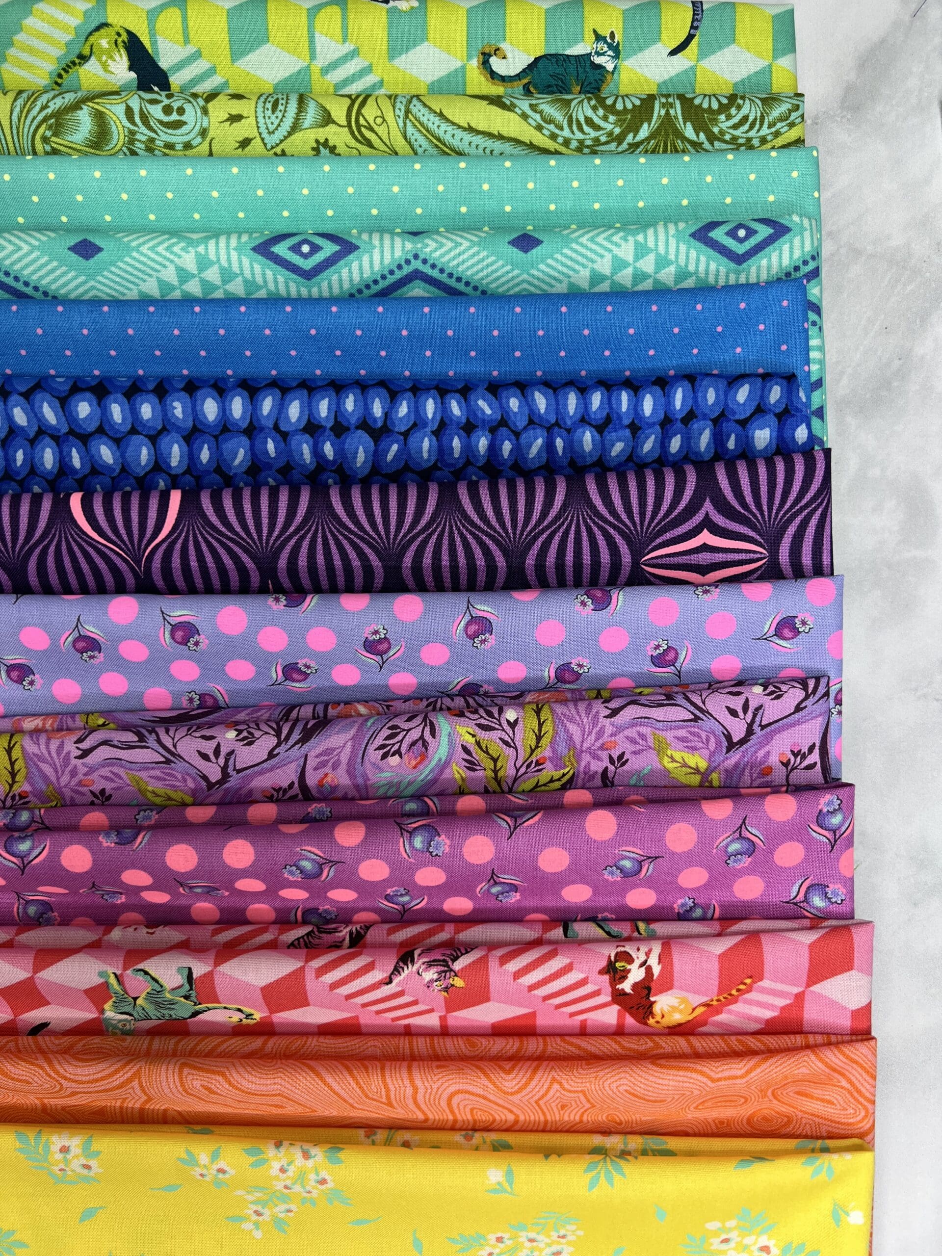 Stack of colorful patterned fabrics in blue, purple, and pink hues.