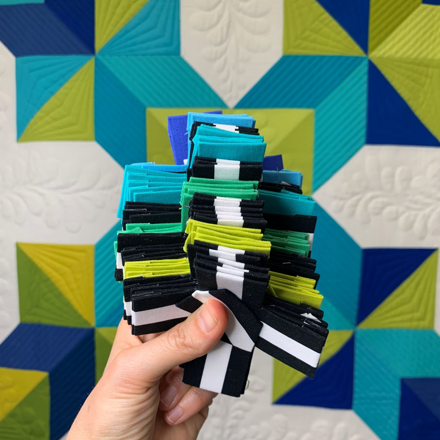 A person holding up a stack of fabric squares.