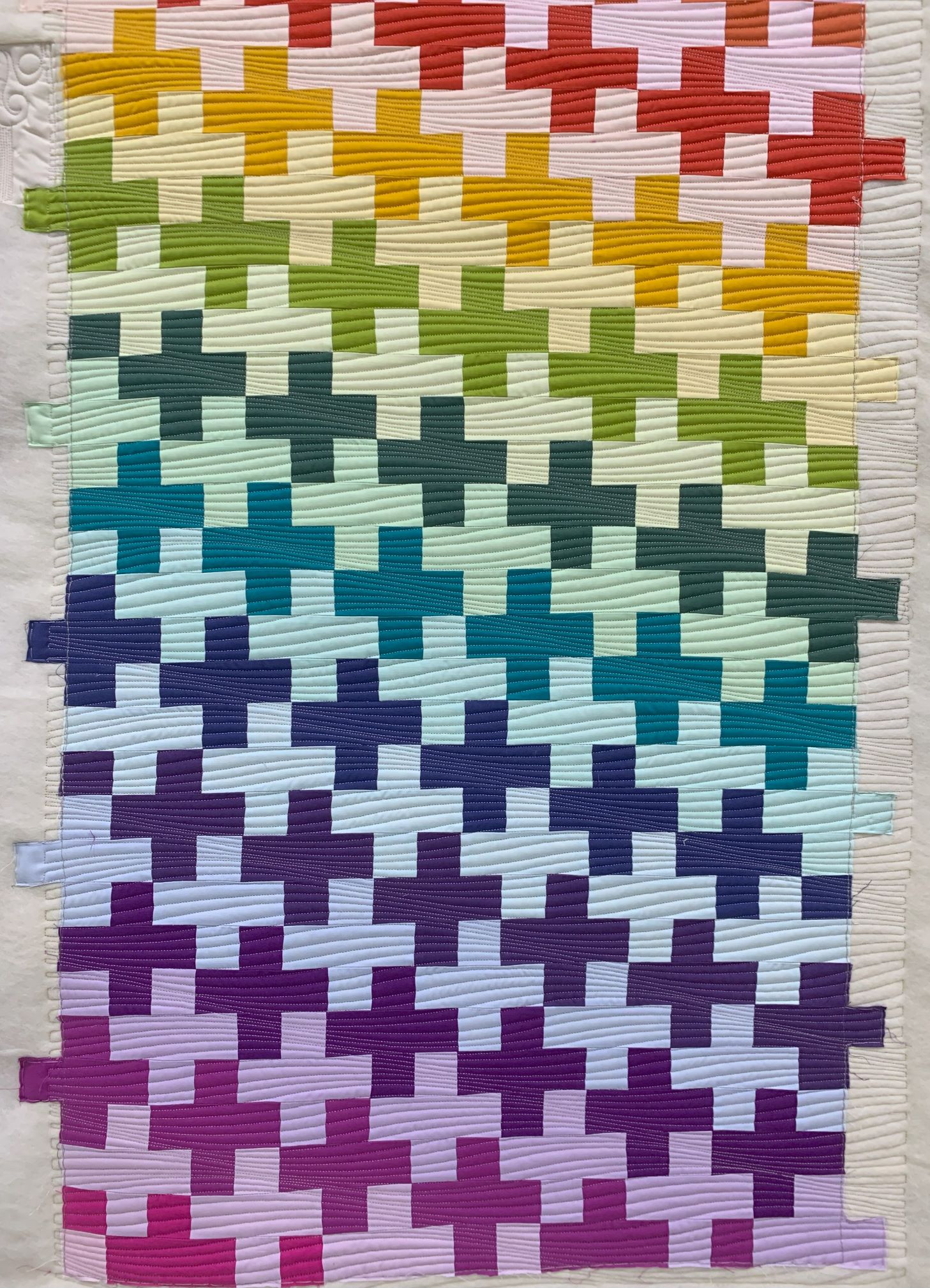A rainbow colored quilt with crosses on it.