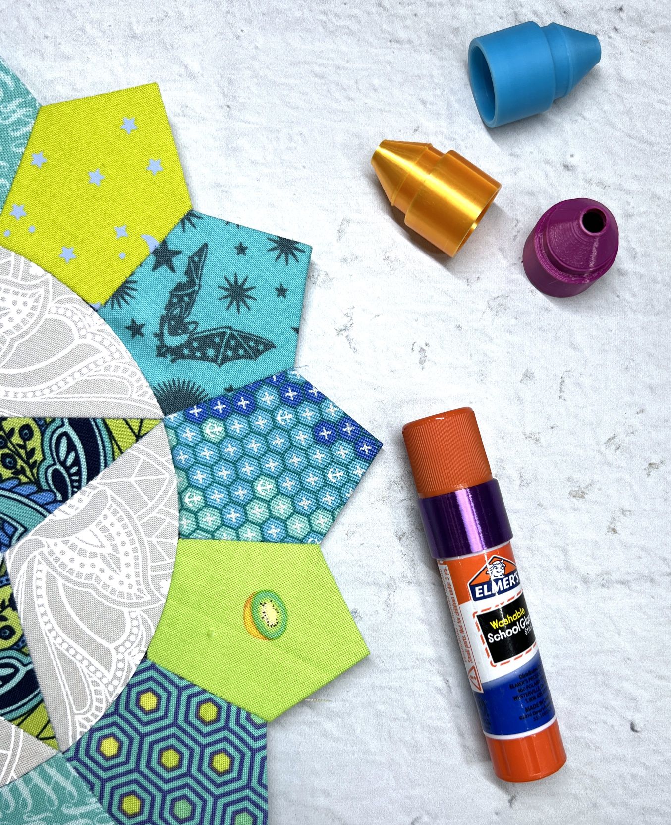 Crafting materials including glue stick, fabric hexagons, and sewing tools on a table.