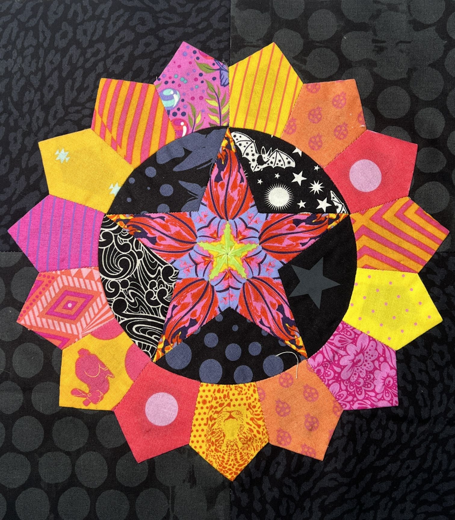 Colorful quilt block with star pattern in warm tones on black background.
