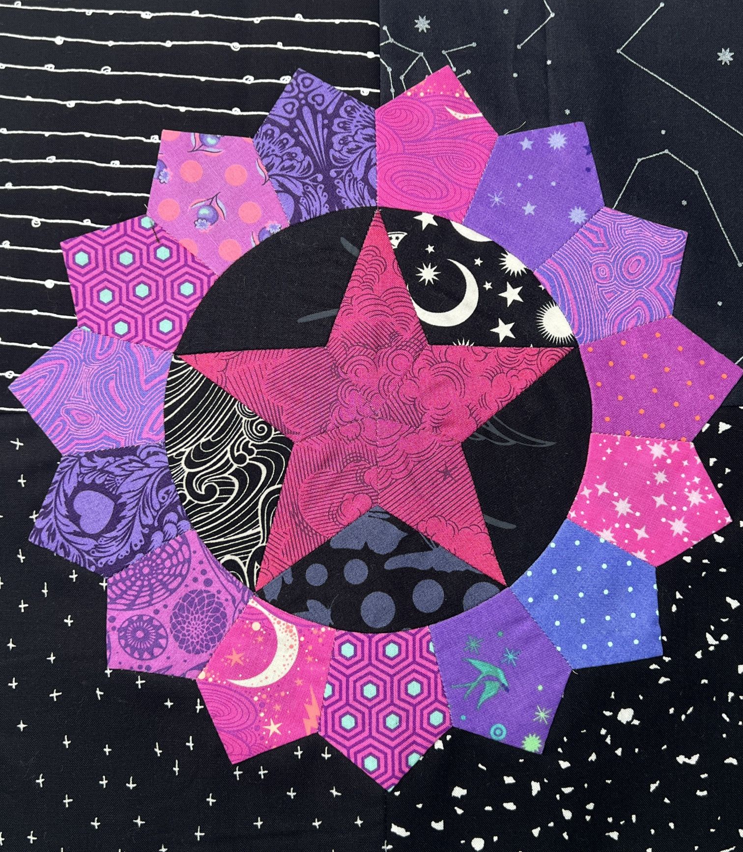 A vibrant quilt block with star and flower patterns in pink, purple, and black.