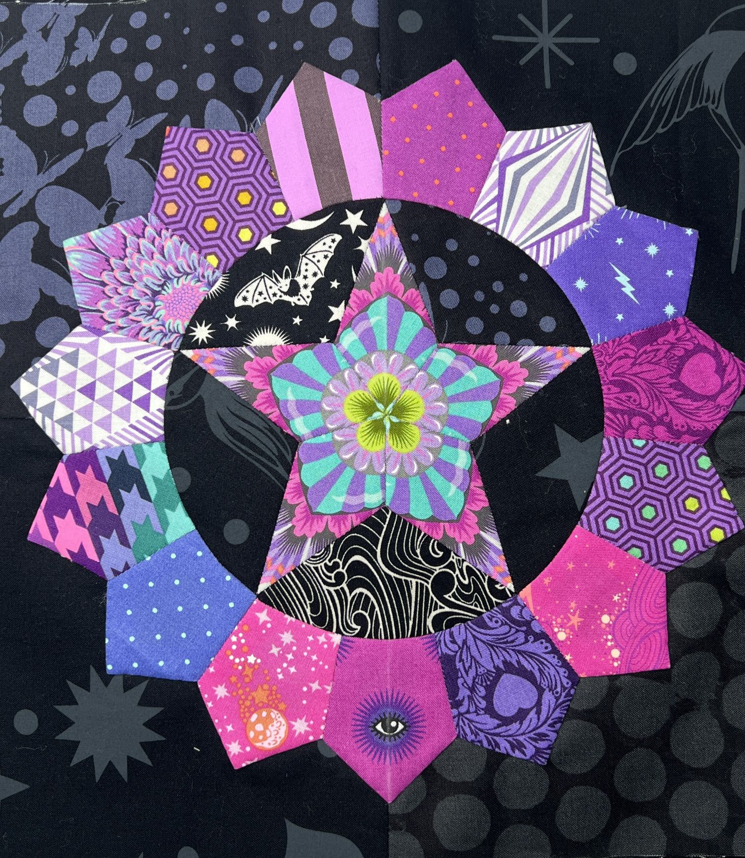 A colorful, patterned fabric starburst quilt with a black center.