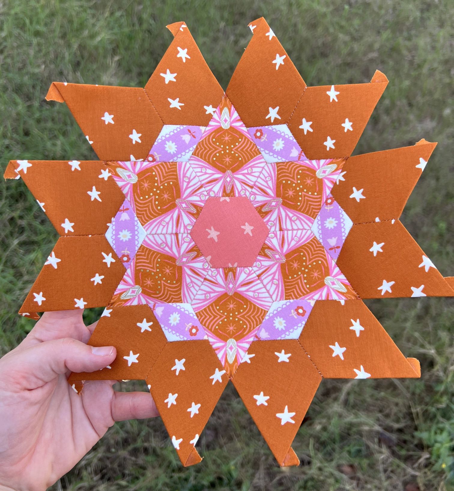 Hand holding a colorful, star-shaped mandala on grass.