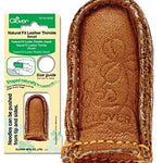 A brown leather thimble with a stitch on it.