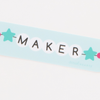 White beads spelling 'MAKER' with star-shaped beads on a blue strip.