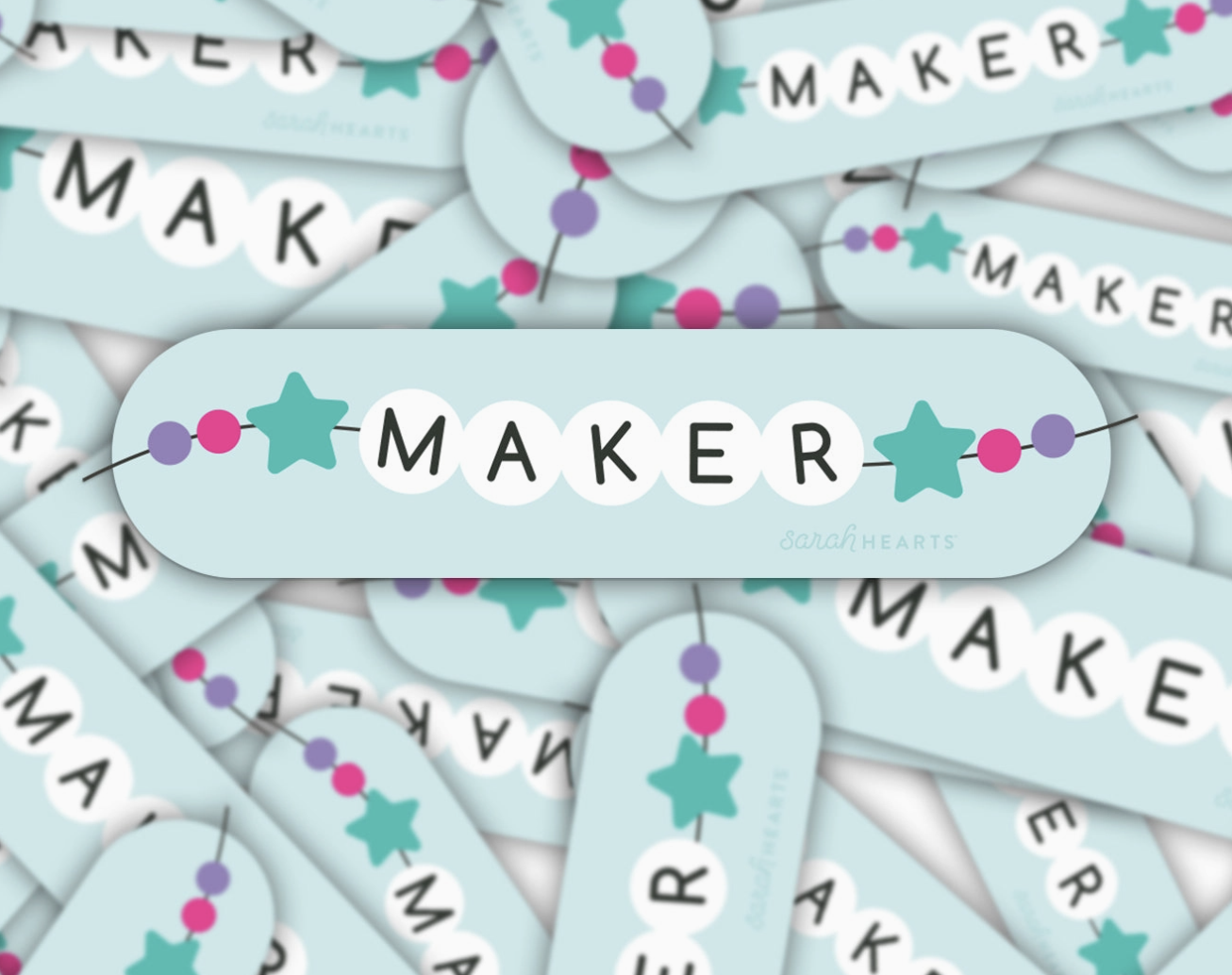 Close-up of pastel-colored earrings with the word 'MAKER'.