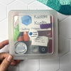 A quilting starter kit with essential tools in a clear plastic case.