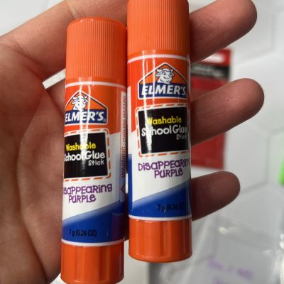 Two Elmer's purple washable school glue sticks held in a hand.