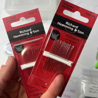 Two packs of red sewing needles with white thread holders.