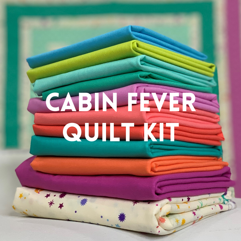 A stack of folded fabric with the words cabin fever quilt kit in front.
