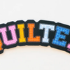 Colorful embroidered word 'QUILTER' on black fabric.