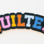Colorful embroidered word 'QUILTER' on black fabric.