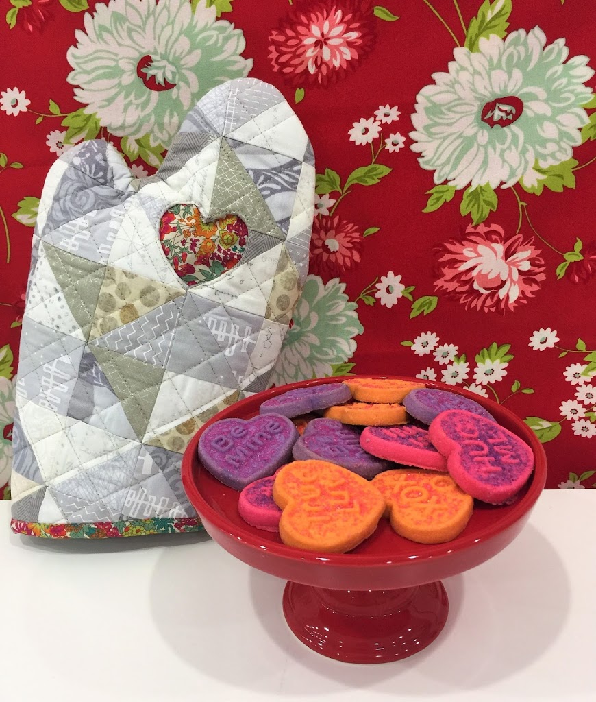 A red bowl of cookies and a quilted heart shaped bag.