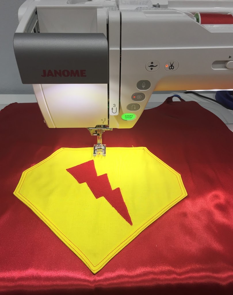 A sewing machine is cutting out the fabric for a superman logo.