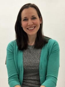 Smiling woman in turquoise sweater, seated indoors.