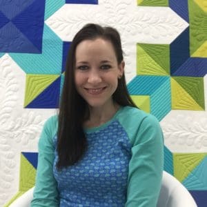 A woman sitting in front of a quilt.