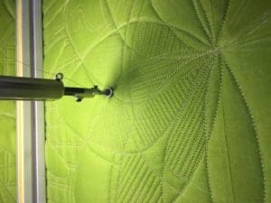 A green quilt being worked on a sewing machine.