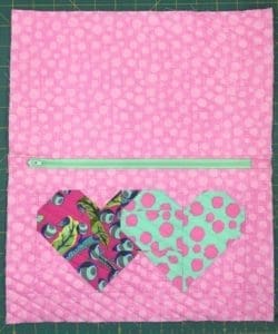 A pink and green heart quilt with a zipper.