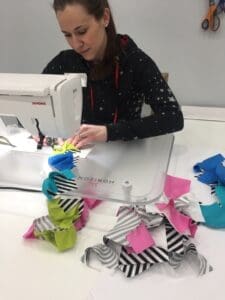 A woman sewing paper bags on top of a table.