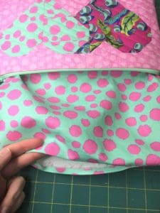 A person is sewing on the fabric of a bag.