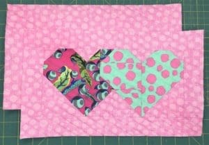 A pink and green heart quilt on top of a table.