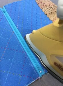 A yellow iron is on the ground next to blue fabric.