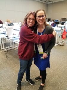 Two women hugging in a room with tables and chairs.