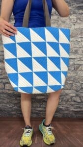 A person standing in front of a brick wall holding onto a blue and white quilt.
