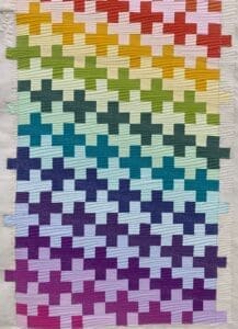 A rainbow colored quilt with crosses on it.