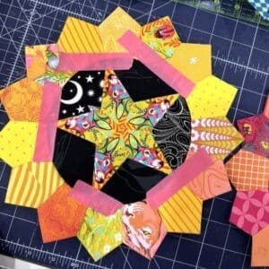 Colorful patchwork quilt block with star and heart shapes on a cutting mat.