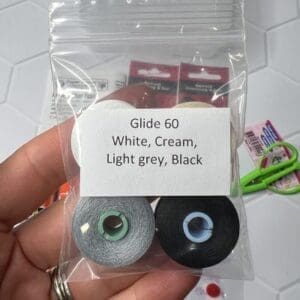 A hand holding a small plastic bag with four colored Glide 60 strings.