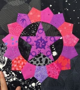 A colorful star-shaped quilt block with pink, purple, and red fabric pieces.