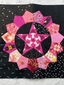 Colorful quilted star with pink and purple petals on a black background.