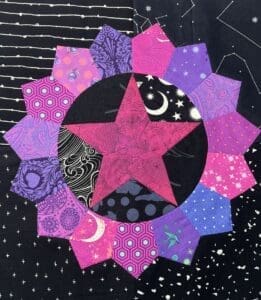 A vibrant quilt block with star and flower patterns in pink, purple, and black.