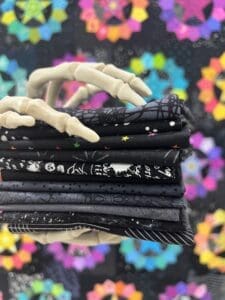 Stack of black fabric pieces with white patterns and a pair of scissors on top.