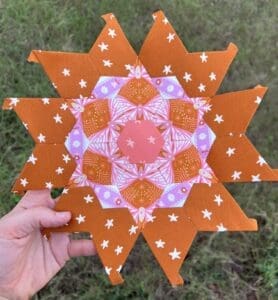 Hand holding a colorful, star-shaped mandala on grass.